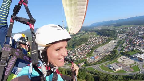 Happy-couple-enjoy-tandem-paragliding-over-lush-field,-Slovenj-Gradec
