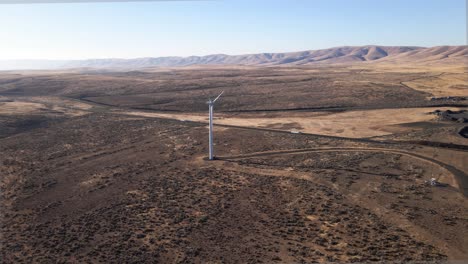 Slow-aerial-pull-of-a-lone-electric-wind-turbine-next-to-a-long-desert-highway