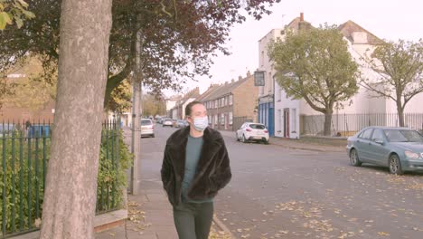 Female-wearing-a-medial-facemask-looking-at-phone-whilst-walking-on-a-street-towards-camera