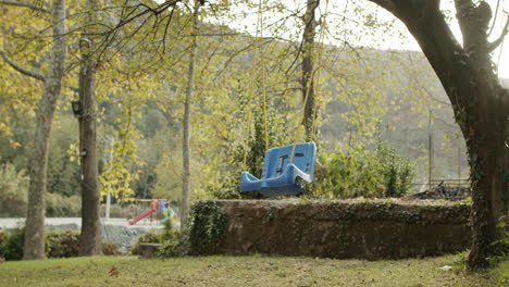 Wide-Shot-of-a-Lonely-Blue-Swing-Hanging-from-the-Tree-with-Rustic-Ropes,-Swinging-in-Depression-in-slow-mo