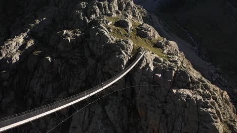 Rotating-shot-of-a-single-person-conquering-the-fear-of-heights-by-walking-on-a-narrow-and-long-suspension-bridge-during-a-hike-in-the-Swiss-alps-on-a-hot,-sunny-day