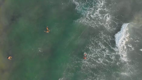 Rotating-aerial-top-down-view-of-tourists-excited,-enjoying-and-playing-with-the-waves-in-the-middle-of-the-sea