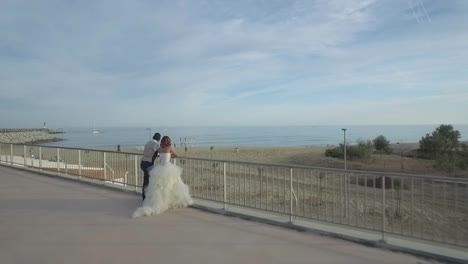 Flying-Over-Romantic-Bride-and-Groom-Looking-Out-Beach-and-Sea-View,-Aerial