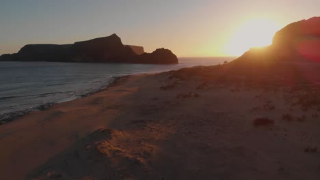 Rückwärtsaufnahme-Aus-Der-Luft,-Sonnenuntergangslichter-Am-Calheta-Strand,-Inselchen-Als-Hintergrund