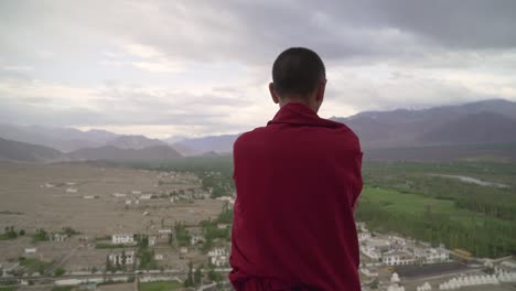 A-tibetan-buddhist-monk-contemplats-while-staring-out-towards-a-beautiful-Himalayan-landscape-during-sunrise
