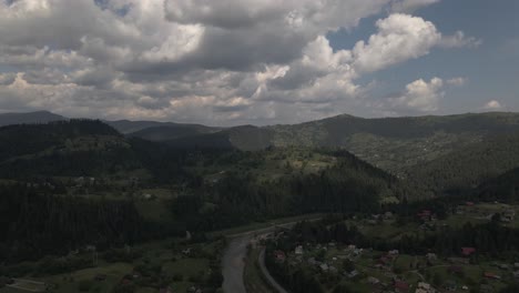 Flug-über-Einen-Fluss-In-Richtung-Bewaldeter-Hügel-In-Einer-Landschaft,-Die-Von-Kleinen-Häusergruppen-Und-Ackerlandstücken-Bedeckt-Ist