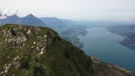 Luftaufnahme,-Die-Den-Gipfel-Des-Morgenberghorns-In-Der-Schweiz-Umrundet-Und-Die-Steilen-Und-Dramatischen-Hänge-Direkt-Neben-Einem-Blauen-Und-Türkisfarbenen-Fluss-Zeigt,-Der-Neben-Kleinen-Dörfern-In-Der-Ferne-Fließt