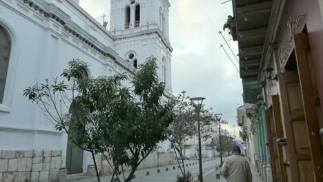 Amazing-white-church-steeple-on-an-over-cast-day-tilting-down-to-reveal-old-men-walking-on-the-street-Ecuador