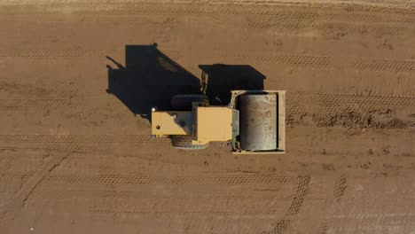 Top-down-following-aerial-shot-of-a-Bulldozer-Roller-compacting-dirt-on-a-sunny-day