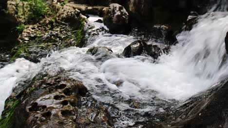 Agua-Que-Cae-Suavemente-En-Cascada-Desde-El-Lecho-De-Un-Pequeño-Arroyo-Que-Pasa-Sobre-Las-Rocas-Y-Luego-Continúa-Cayendo-Sobre-Otro-Borde