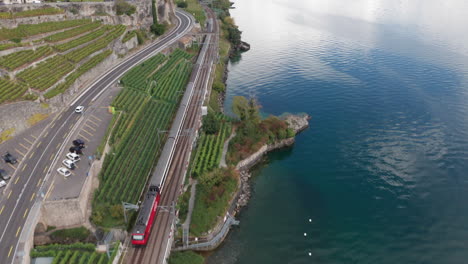 aerial-of-train-driving-through-Swiss-countryside,-tilting-up-and-revealing-beautiful-lake-with-distant-mountains