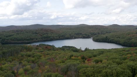 Pull-back-aerial-view-of-a-calm-lake-in-a-dense-forest-in-autumn