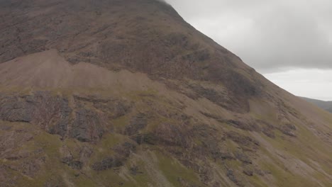 advance-drone-shot-in-isle-of-skye-highlands-scotland,-close-view-of-a-tall-mountain-with-green-grass-and-rocks-in-a-cloudy-day