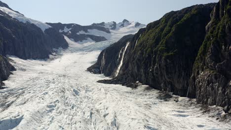 Aerial-View-of-Glacier-and-Glacial-Waterfall-Falling-on-Ice-on-Sunny-Day,-Alaska-USA,-Pull-Up-Drone-Shot