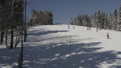 Kope-ski-resort-in-Slovenia-with-many-skiers-going-downhill-near-snow-machines,-Aerial-dolly-in-shot