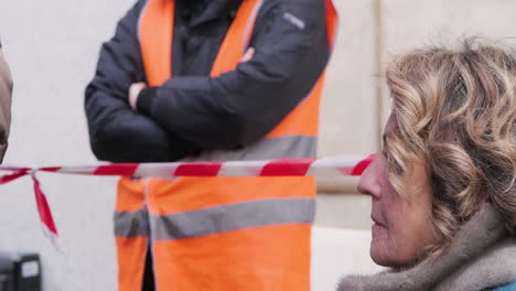 Serious-Old-Blonde-Lady-Listening-and-Participating-in-the-Protest-in-Piazza-Milano-with-People-and-Security-in-the-Background