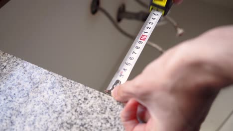 Man-Uses-Steel-Tape-Measure-In-Measuring-Size-Of-Countertop-In-The-Kitchen---close-up