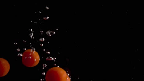 Tomates-Cayendo-Al-Agua-En-Cámara-Superlenta,-Fondo-Negro,-Muchas-Burbujas-De-Aire,-4k240fps