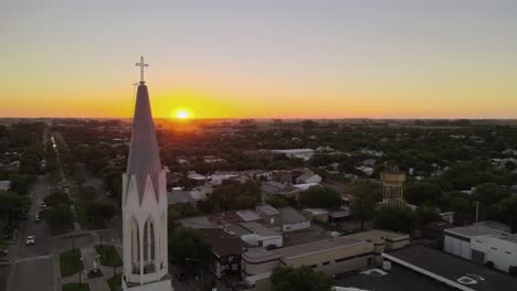 Aerial-parallax-shot-of-a-church-bell-tower-on-a-small-town-at-sunset