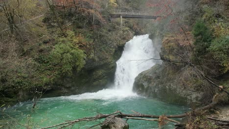 Langsamer-Schwenk,-Kraftvoller-Wasserfall,-Grüner-Wald,-Türkisfarbenes-Wasser,-Brücke,-Tag