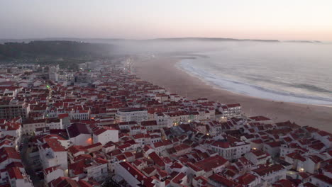 Aerial-View-Of-Nazare-Beach-Riviera-With-Cityscape-Of-Nazare-Town-In-Portugal---aerial-drone-shot