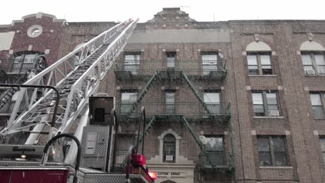 Fire-engine-ladder-reaching-for-Brooklyn-rooftop-supervised-by-Firefighters-under-snowfall---Wide-tilt-up-shot