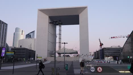 La-Defense-Great-Arch-and-metro-entrance-with-few-people-walking-by-during-early-morning-in-winter