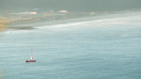 Plätscherndes-Wasser-Mit-Einem-Schiff,-Das-Während-Eines-Dunstigen-Morgens-Am-Strand-Von-Nazare,-Portugal,-Segelt
