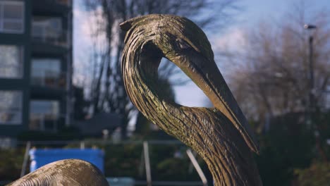 A-close-up-of-blue-heron-sculpture-in-the-busy-city-landscape-with-a-blurry-background-of-buildings-blue-sky-tree