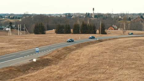 Drone-footage-of-electric-Porsche-Taycan-cars-driving-in-country-road,-Lithuania