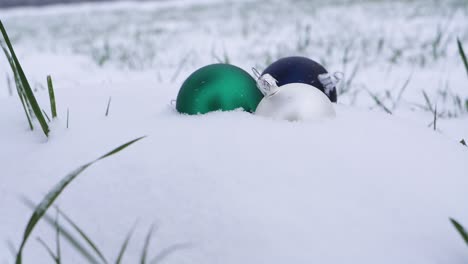 Close-up-Slow-motion-shot-of-multicolored-christmas-balls-falling-down-and-landing-in-soft-snow-outdoors-during-winter