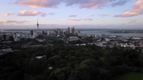Auckland-Domain-park,-sky-tower-and-cityscape-under-wispy-colorful-clouds,-dolly-in