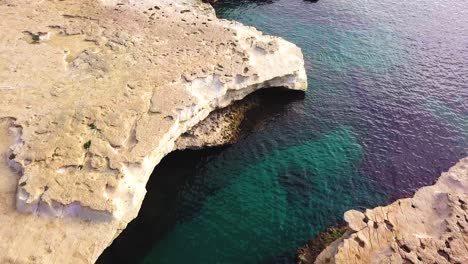 Ein-Flug-Am-Frühen-Morgen-über-Den-Malerischen-St.-Peters-Pool-Auf-Malta-Mit-Blick-Auf-Die-Goldenen-Sandsteinfelsen-Und-Das-Kristallklare-Blaue-Wasser-Des-Mittelmeers