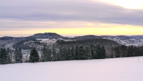 Sunrise-over-a-winter-landscape---panning-shot-over-a-beautiful-snowy-white-field-with-hills-in-the-background