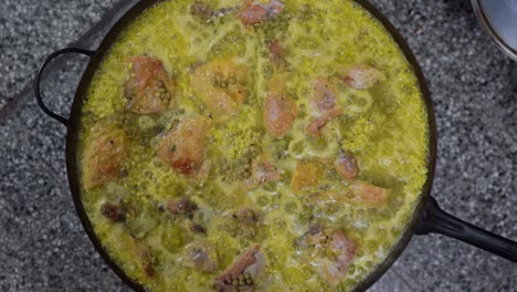 Draufsicht-Auf-Die-Köstliche-Spanische-Paella-Mit-Grünen-Erbsen,-Hühnchen-Und-Reis,-Die-In-Einer-Großen-Pfanne-In-Der-Küche-Köchelt,-Nahaufnahme