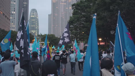 Multitud-De-Manifestantes-Ondeando-Banderas-Mientras-Caminan-Por-La-Calle-En-Tokio,-Japón