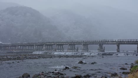 Snow-Fall-over-Togetsu-Kyo-Bridge-and-Katsura-River,-Arashiyama-in-Background