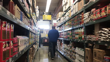 A-Man-Shopper-With-Push-Cart-Walking-Through-Grocery-Aisle-At-Smart-Foodservice-Warehouse-In-Coos-Bay,-Oregon