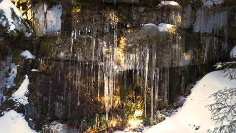 Lange-Eiszapfen-Hängen-An-Einer-Feuchten-Bergwand-Aus-Stein,-Verschneit,-Tschechien