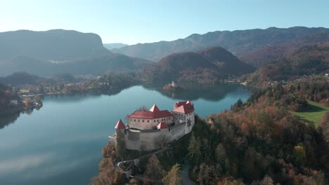 Aerial-View-of-Lake-Bled-Castle-flying-from-left-to-right-with-the-stunning-lake-bled-and-lake-bled-island-and-church-in-the-background-on-a-autumn-morning-in-Slovenia
