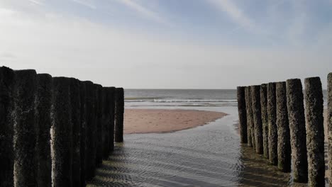 Row-Of-Old-Wooden-Piles-On-Seashore-With-Splashing-Waves-In-Brouwersdam,-Netherlands