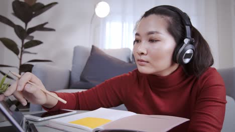 Asian-woman-on-redshirt-using-a-tablet-with-headphone-for-meeting-online-at-home
