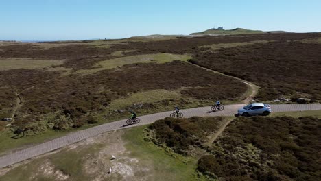 Active-mountain-biking-family-riding-mountain-bikes-on-colourful-England-summit-trail-Aerial-view-tracking-cross-country