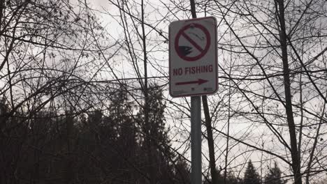 No-fishing-sign-posted-at-a-public-park-image-of-hook-and-fish-black-and-white-city-government-sign-trees-ky-clouds-in-background