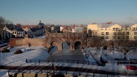 Aerial-snow-landscape-of-frozen-over-river-with-medieval-Berkelpoort-boat-portal-revealing-the-wider-the-Dutch-historic-cityscape-in-the-background