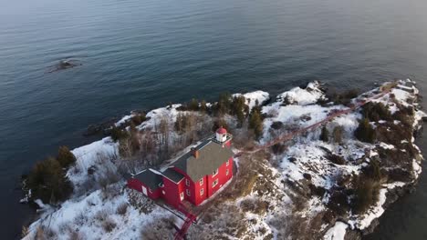 Red-Lighthouse-located-in-Marquette,-Michigan-in-winter-with-rotating-drone-shot