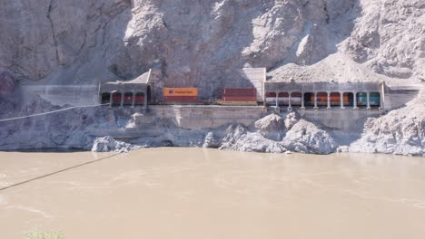 Muddy-river-swirls-in-front-as-transport-freight-train-passes-tunnels