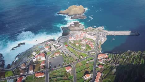 Flying-over-Porto-Moniz-town,-Madeira-island,-Portugal-famous-tourist-vacation-destination-at-sunset-Aerial-view-of-natural-volcanic-swimming-pools-and-huge-waves-crashing-into-the-coastline