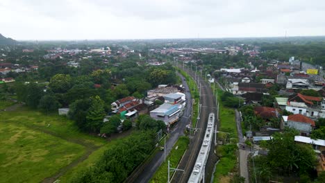 Aerial-tracking-shot-of-electric-train-rides-across-Yogyakarta-city,-Indonesia
