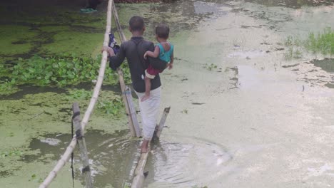 Junge-Trägt-Kind-Im-überfluteten-Wasser-Auf-Einer-Bambusbrücke
